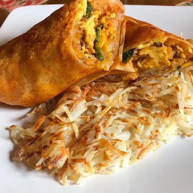 Cut breakfast burrito filled with eggs, meat, cheese, beside crispy hash browns.