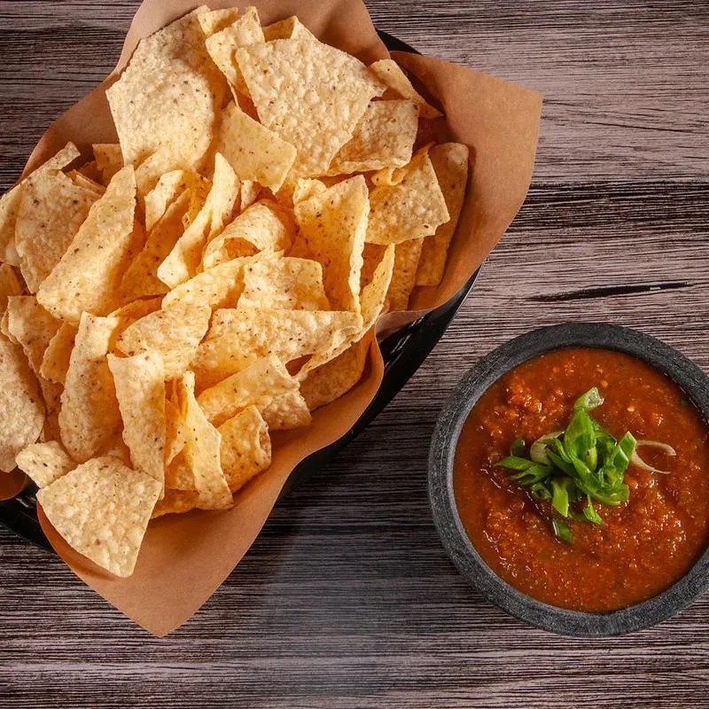 Tortilla chips and chunky red salsa with green onions on wood.