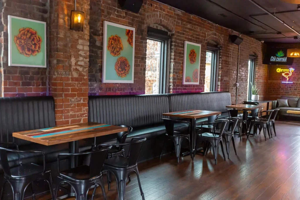 Modern restaurant interior with black booths, exposed brick, and neon signs.