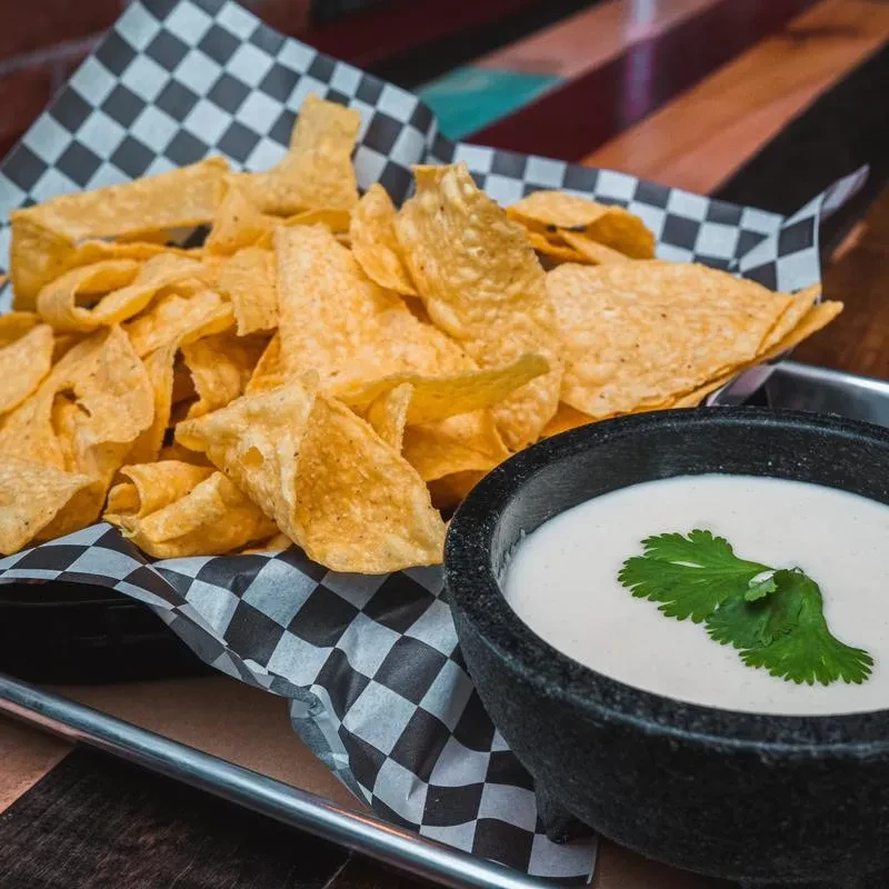 Golden-brown tortilla chips in a basket, creamy dip with cilantro.