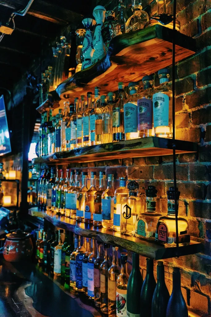 Rustic bar shelves filled with glowing spirits against a brick wall.