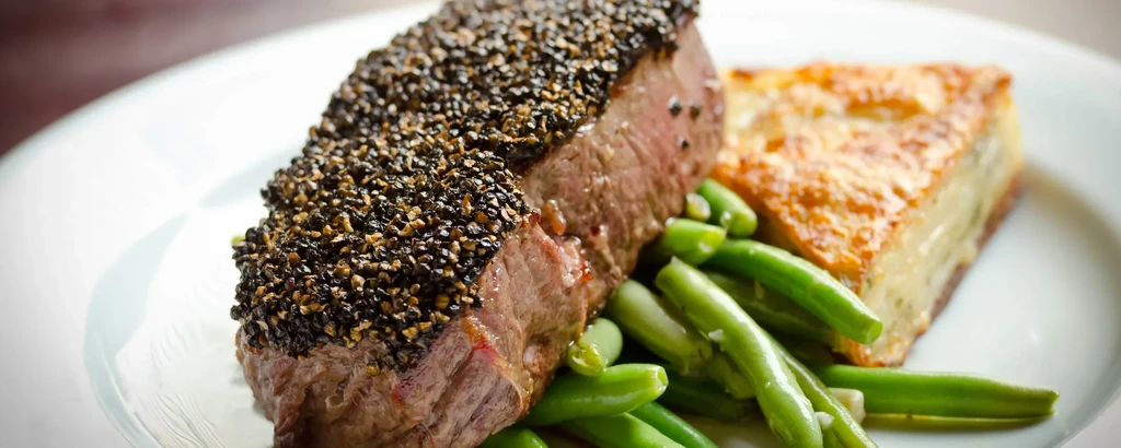 Plated meal with pepper-crusted steak, green beans, and potato gratin.