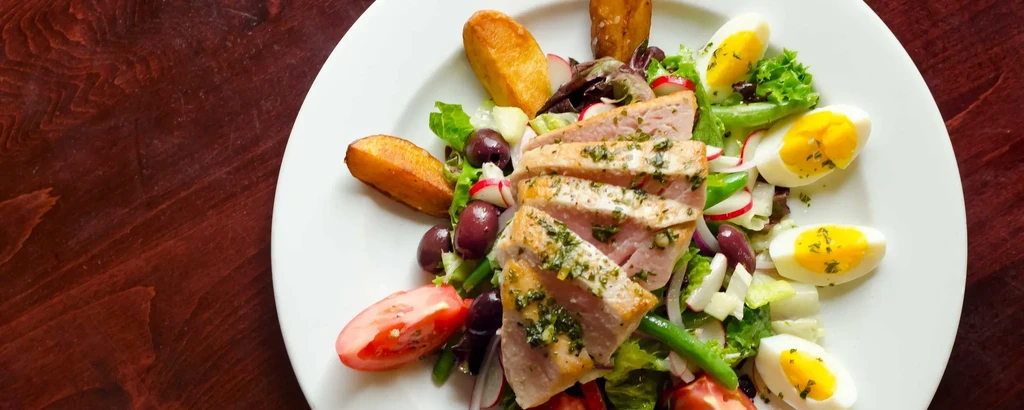 Colorful seared tuna salad with eggs, vegetables, and potatoes.