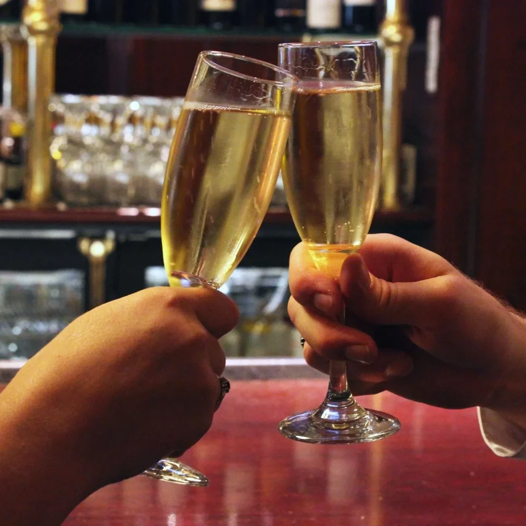 Two hands clinking sparkling golden champagne flutes in a bar.