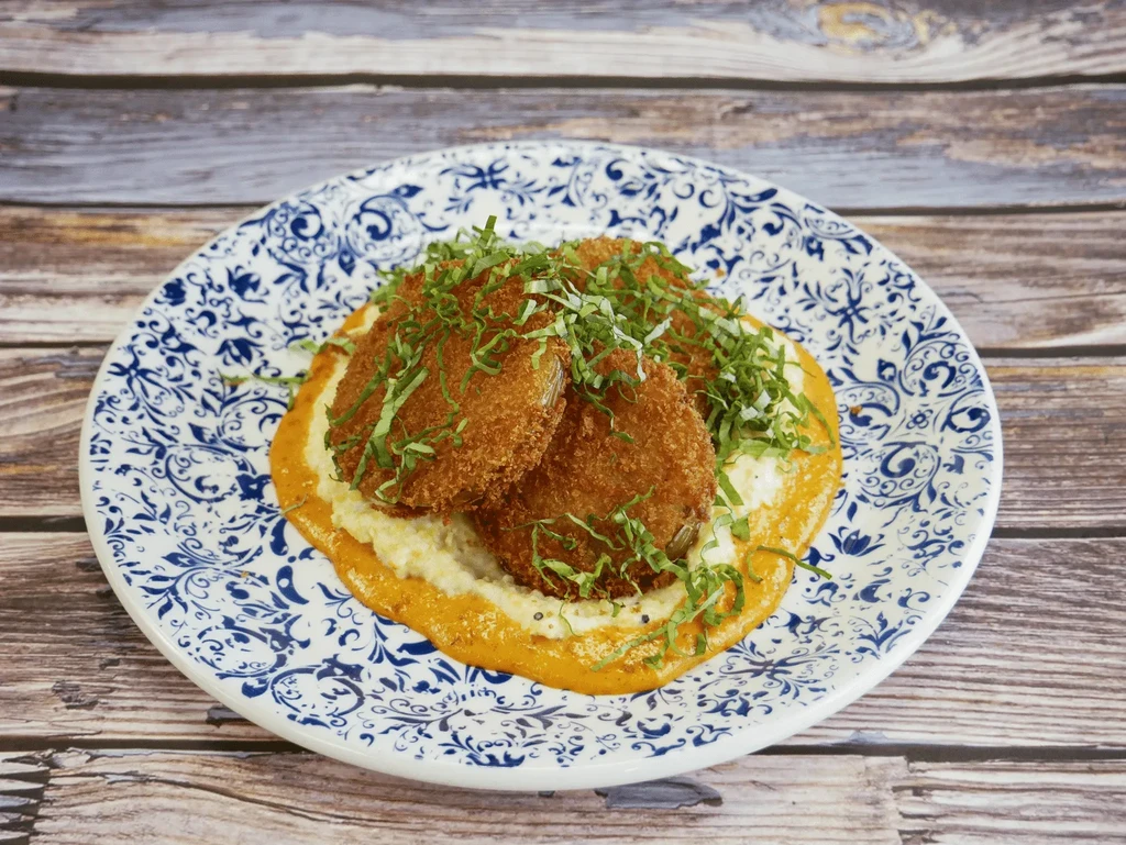 Breaded fried food on creamy grits with orange sauce and green herbs.