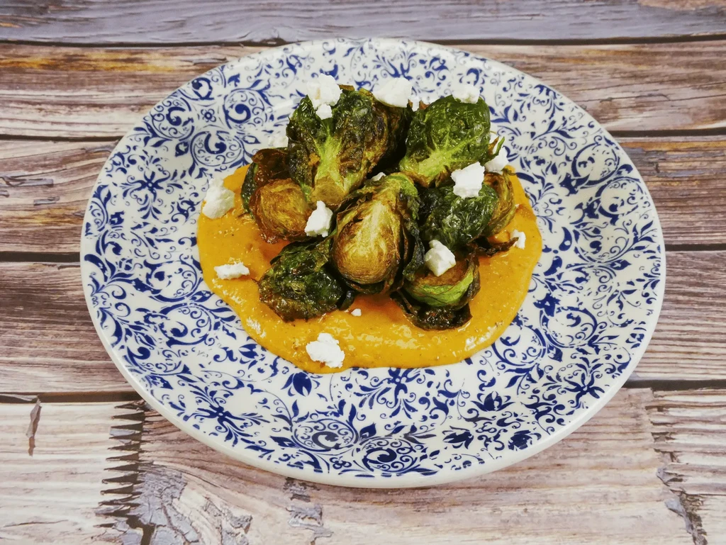 Roasted brussels sprouts, orange puree, cheese, on a patterned plate.