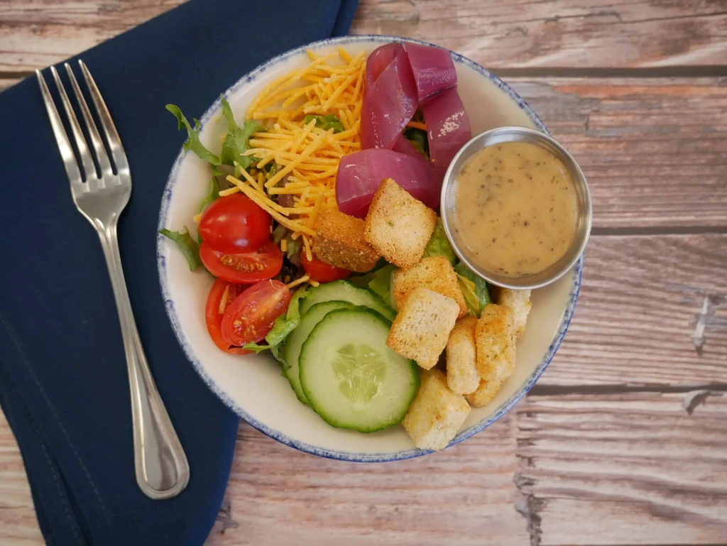 Fresh salad with greens, tomatoes, cheese, croutons, dressing, and fork.