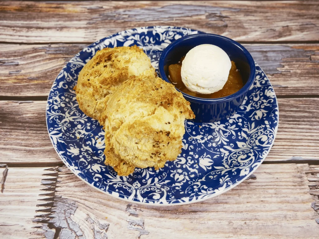 Two golden-brown biscuits, stewed fruit, and ice cream on a blue plate.