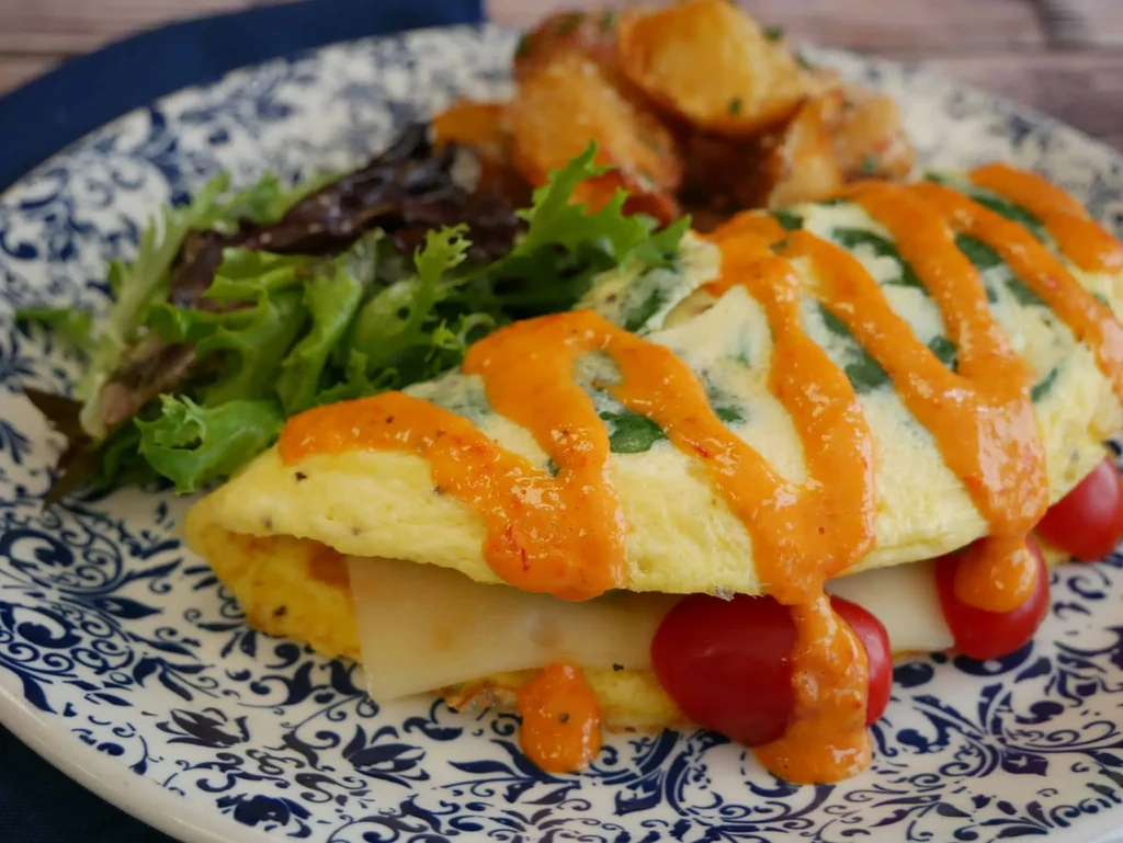 Close-up of an omelet with cheese, tomatoes, sauce, salad, potatoes.
