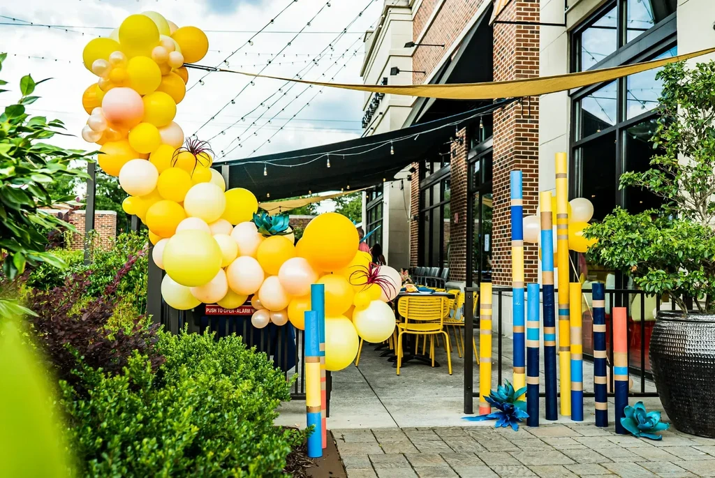Outdoor restaurant patio decorated with a balloon arch and colorful poles.