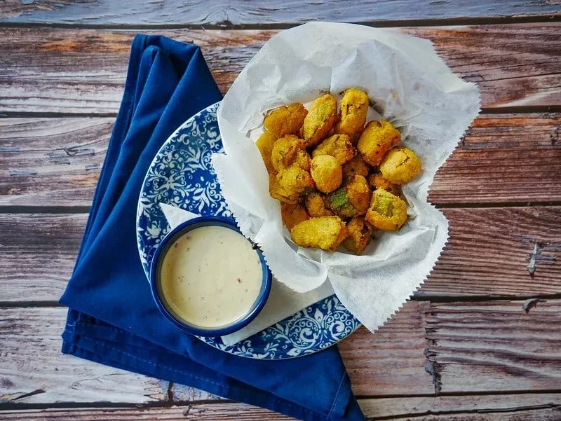 Close-up of golden fried okra with dipping sauce on a wooden table.