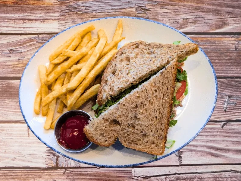 A whole wheat sandwich, golden fries, and ketchup on wood.