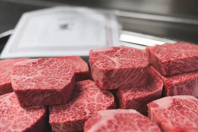 Multiple stacked cuts of raw, intricately marbled beef.