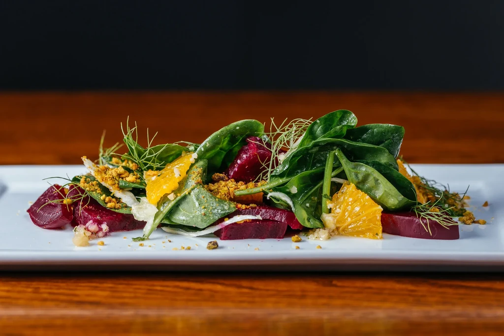 Plated salad with beets, spinach, citrus, and a golden crumb topping.