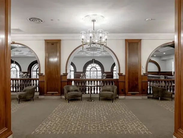 Elegant lounge with high ceiling, chandelier, dark wood, and arched openings.