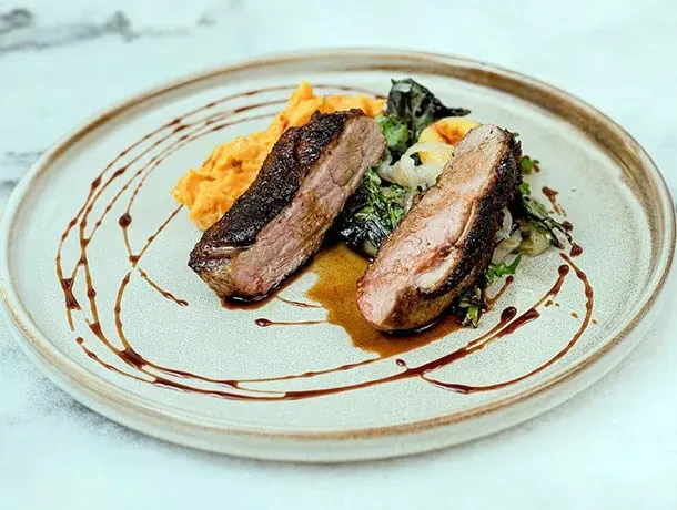Two slices seared meat, dark sauce, orange mash, and greens.