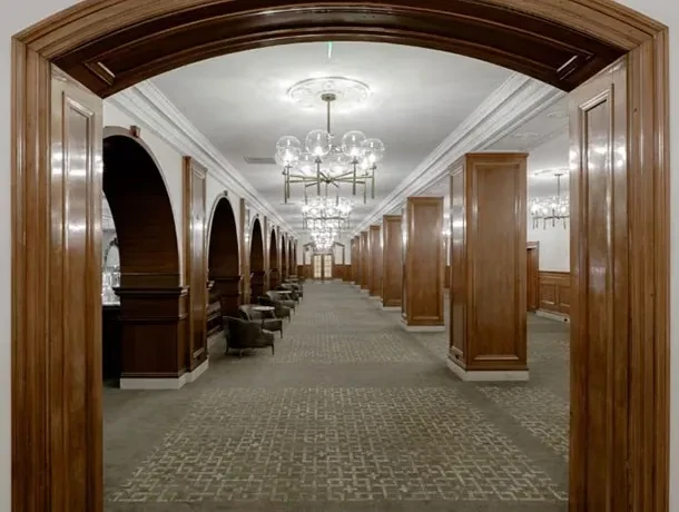 Long, elegant corridor with wooden panels, seating alcoves, and chandeliers.