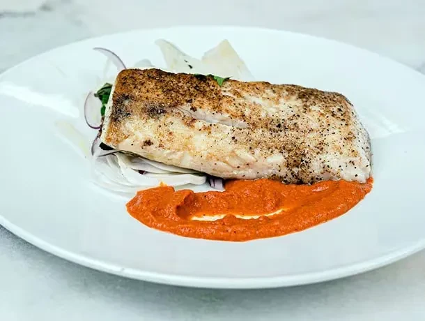 Seared fish with crispy skin, vegetable garnish, and red sauce.