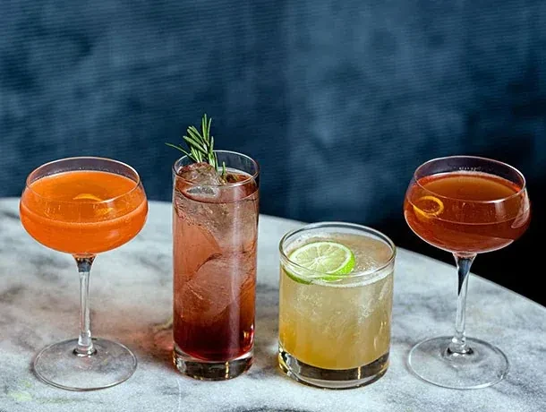 Four distinct cocktails in a row on a light gray surface.
