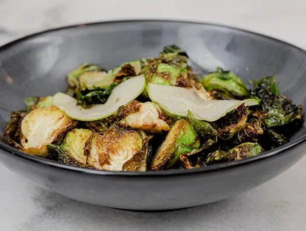 Caramelized roasted Brussels sprouts with apple slices in dark bowl.