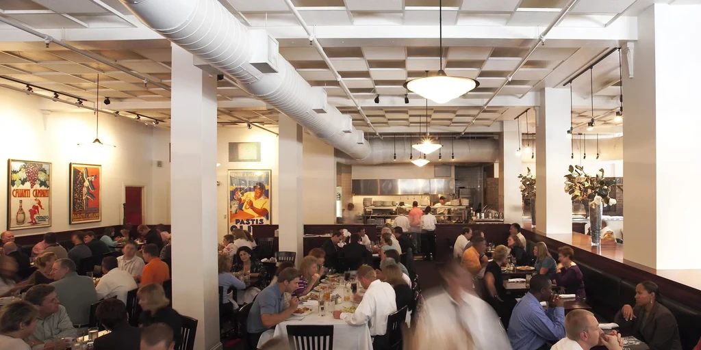 Lively restaurant interior with patrons dining and an open kitchen.