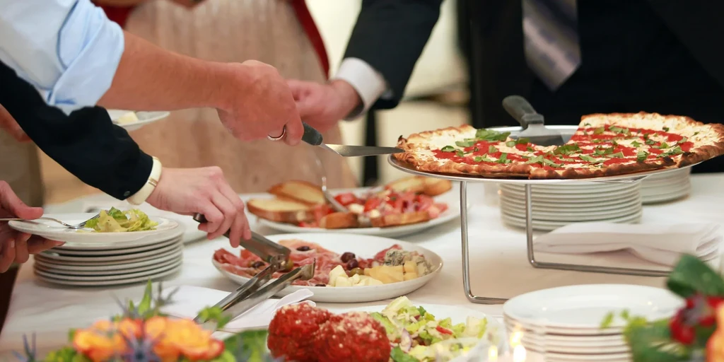 Guests serve themselves pizza, salad, and charcuterie from a buffet.