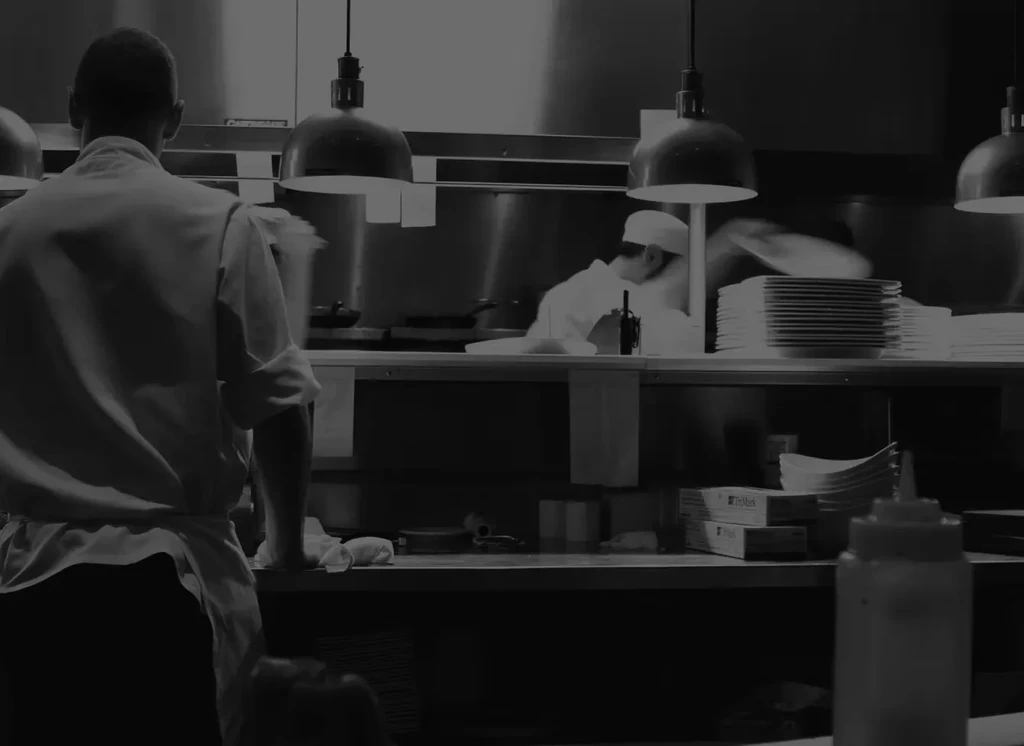 Two chefs work in a busy black and white professional kitchen.