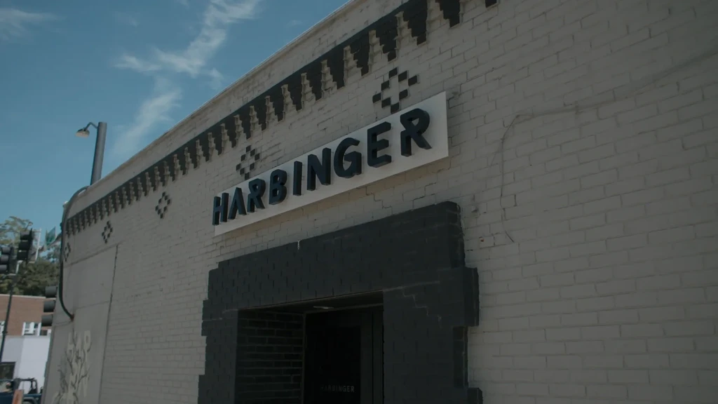 Light brick building facade with HARBINGER sign and dark patterns.