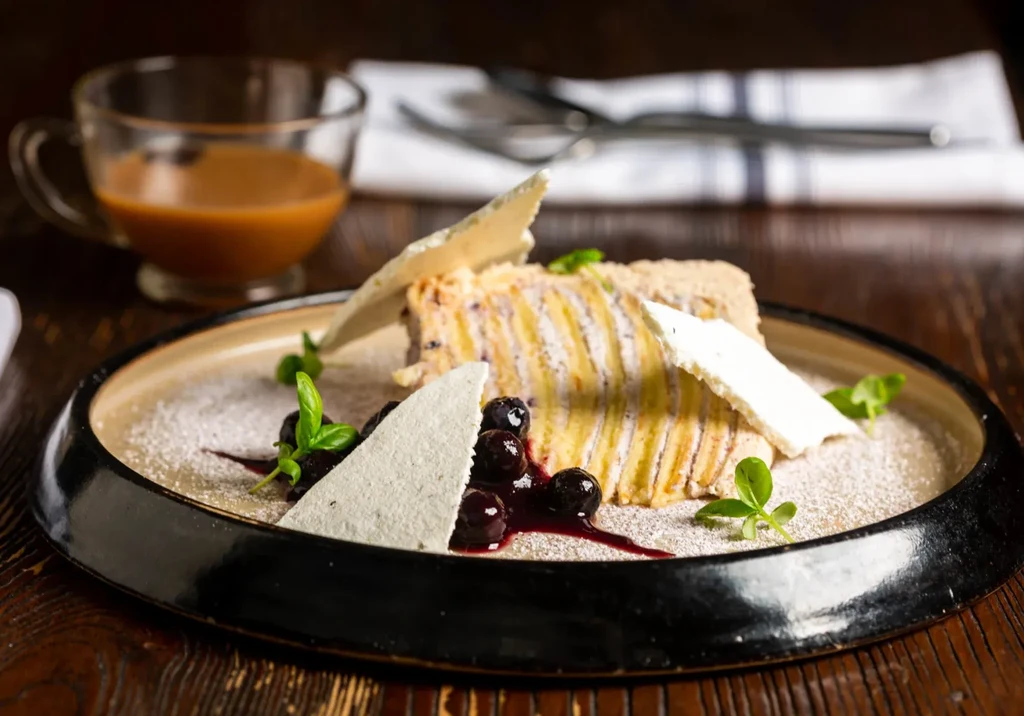 Layered dessert with meringue, purple sauce, blueberries, and powdered sugar.