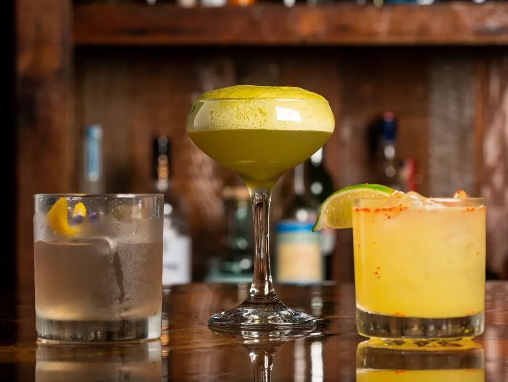 Three distinct, garnished cocktails on a glossy wooden bar counter.