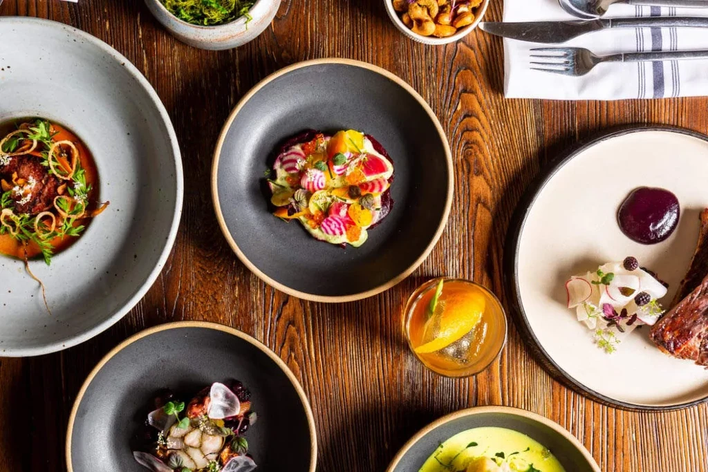 Flat lay of gourmet dishes and a cocktail on a wooden table.