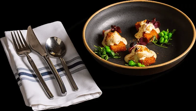 Three golden-fried bites with creamy sauce, garnishes, and cutlery.