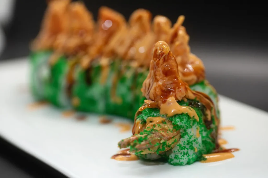 Single green sushi roll with fried shrimp and two sauces.