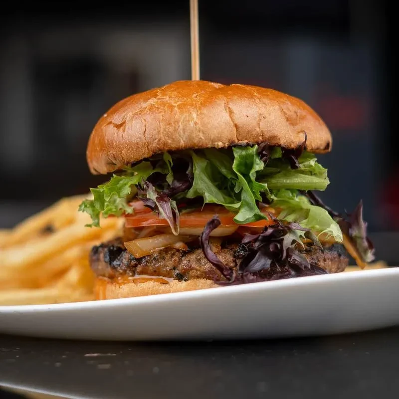 Gourmet burger with grilled patty, fresh vegetables, cheese, and french fries.
