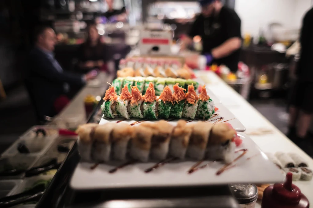 Display of sushi rolls with orange topping and green roe in a restaurant.