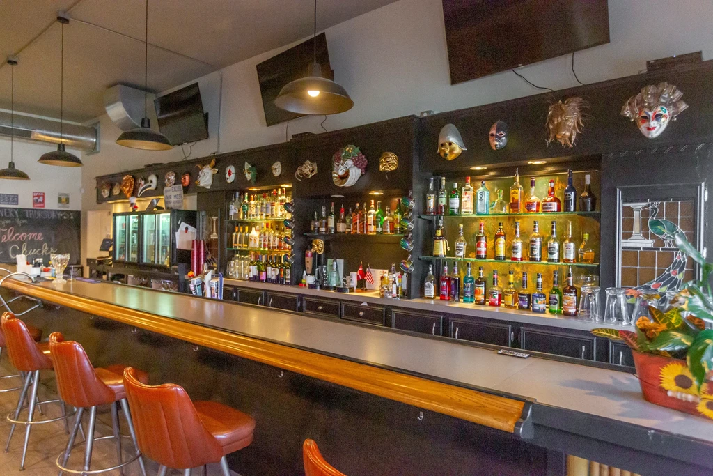 Interior of Chuck's well-stocked bar with counter, stools, and masks.