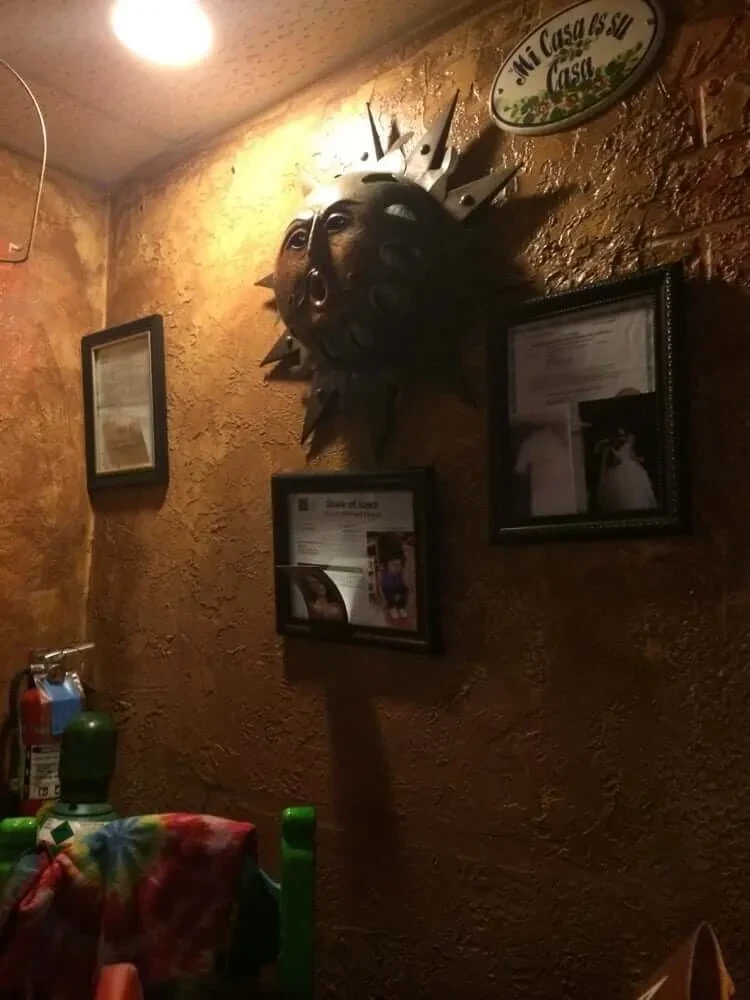 Ornate sun mask, "Mi Casa es su Casa" sign, in a rustic restaurant.