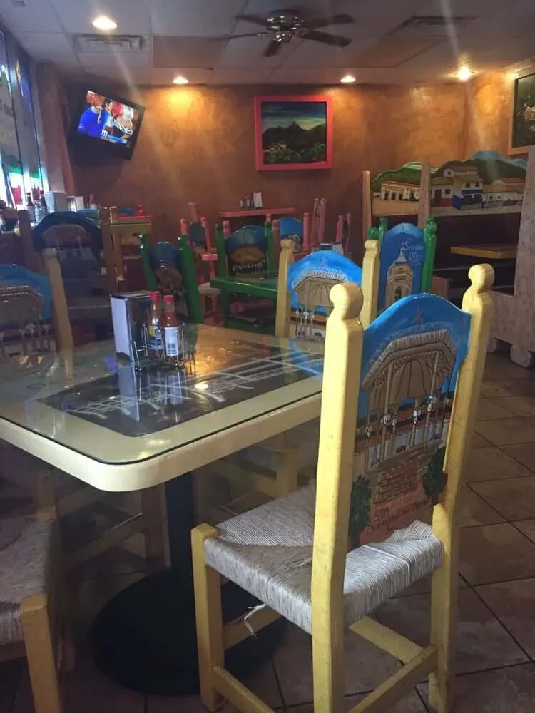 Mexican restaurant interior with colorful hand-painted chairs and earthy walls.
