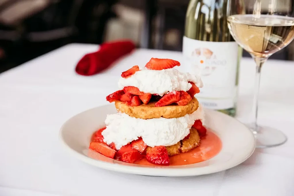 Strawberry shortcake with whipped cream, fresh strawberries, wine glass, and bottle.