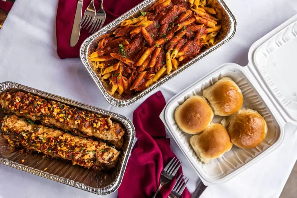 Overhead: penne pasta, seasoned grilled items, and dinner rolls.