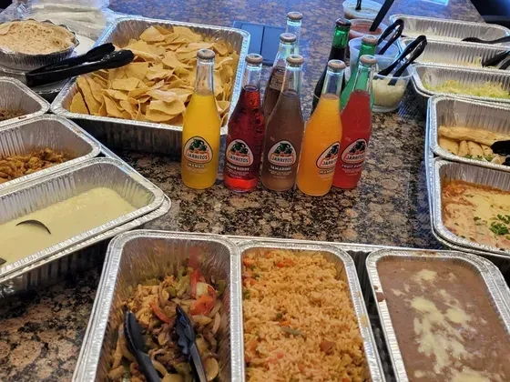 Numerous foil trays of Mexican food, including Jarritos beverages.