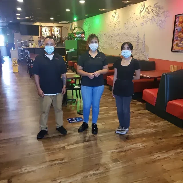 Three masked restaurant staff pose with social distancing signs.