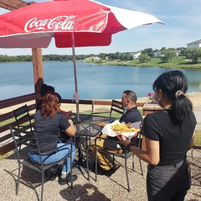 Server delivers food to masked diners on a sunny lakefront patio.