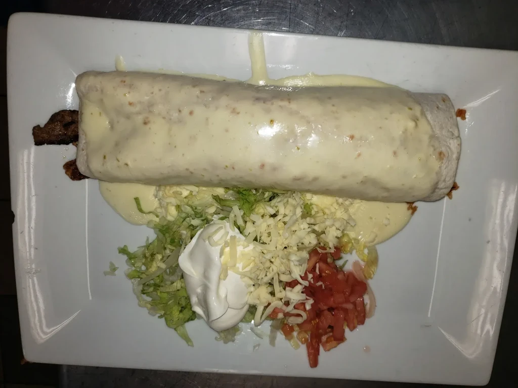 Burrito generously covered in light sauce, with meat and various toppings.