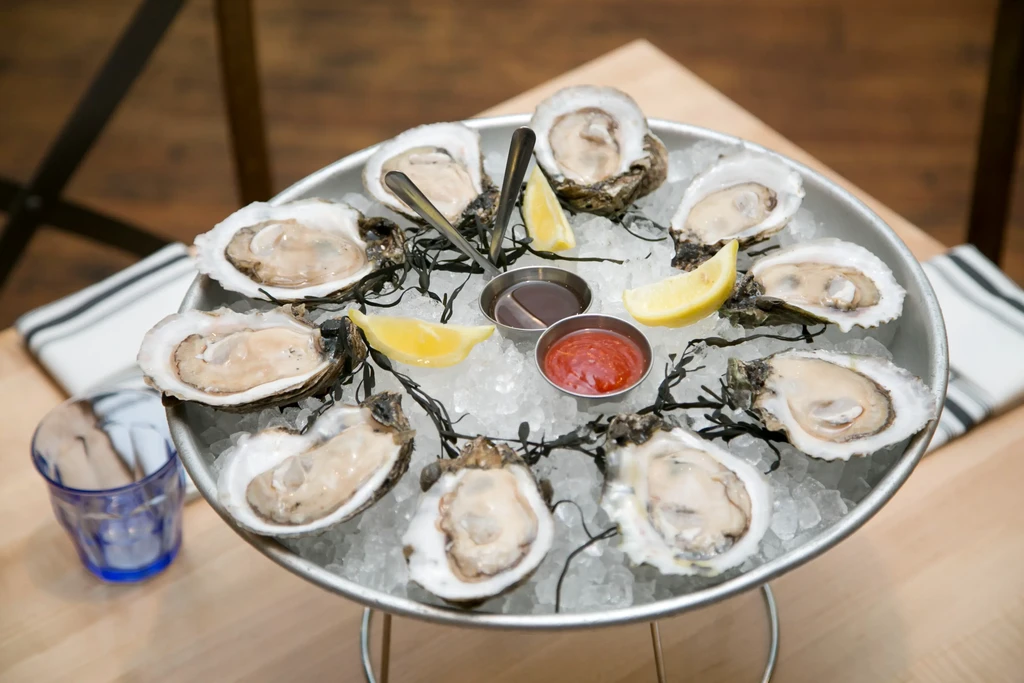 Tiered platter of shucked oysters on ice, lemon, and sauces.