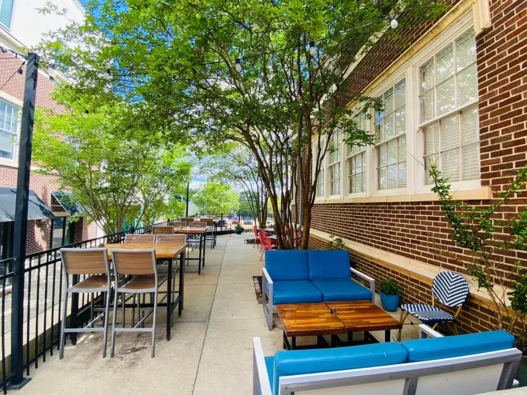 Bright outdoor patio with high-top seating, blue sofas, and string lights.
