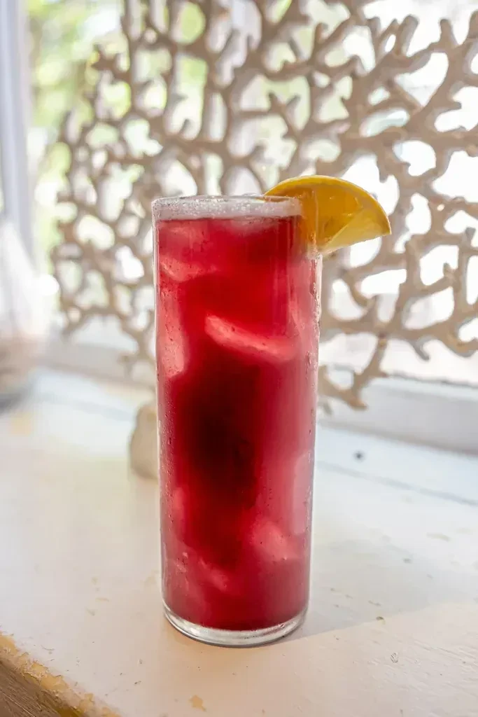 Vibrant red drink with ice, lemon, and intricate background.