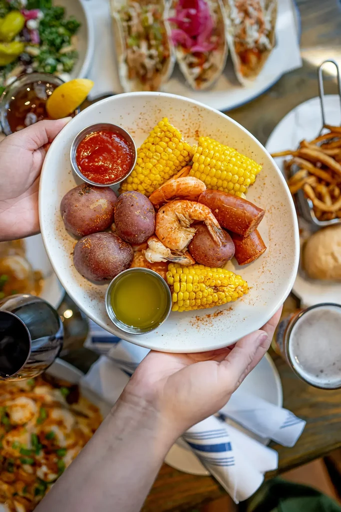 Hands holding a white plate of seafood boil and sauces.