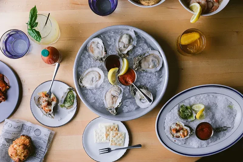 Overhead shot of a table featuring oysters, various seafood, snacks, and drinks.