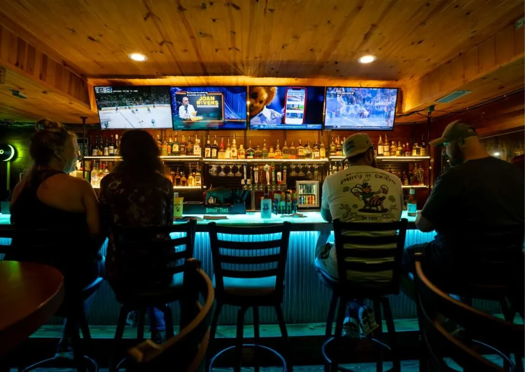 Bar scene with glowing teal counter, liquor bottles, and TVs.